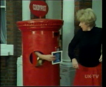 A man dressed as a pillar box offering a letter/stamp combination to a woman.