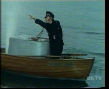 Graeme Garden, dressed in fascist/pirate uniform, stands on a sinking dinghy.